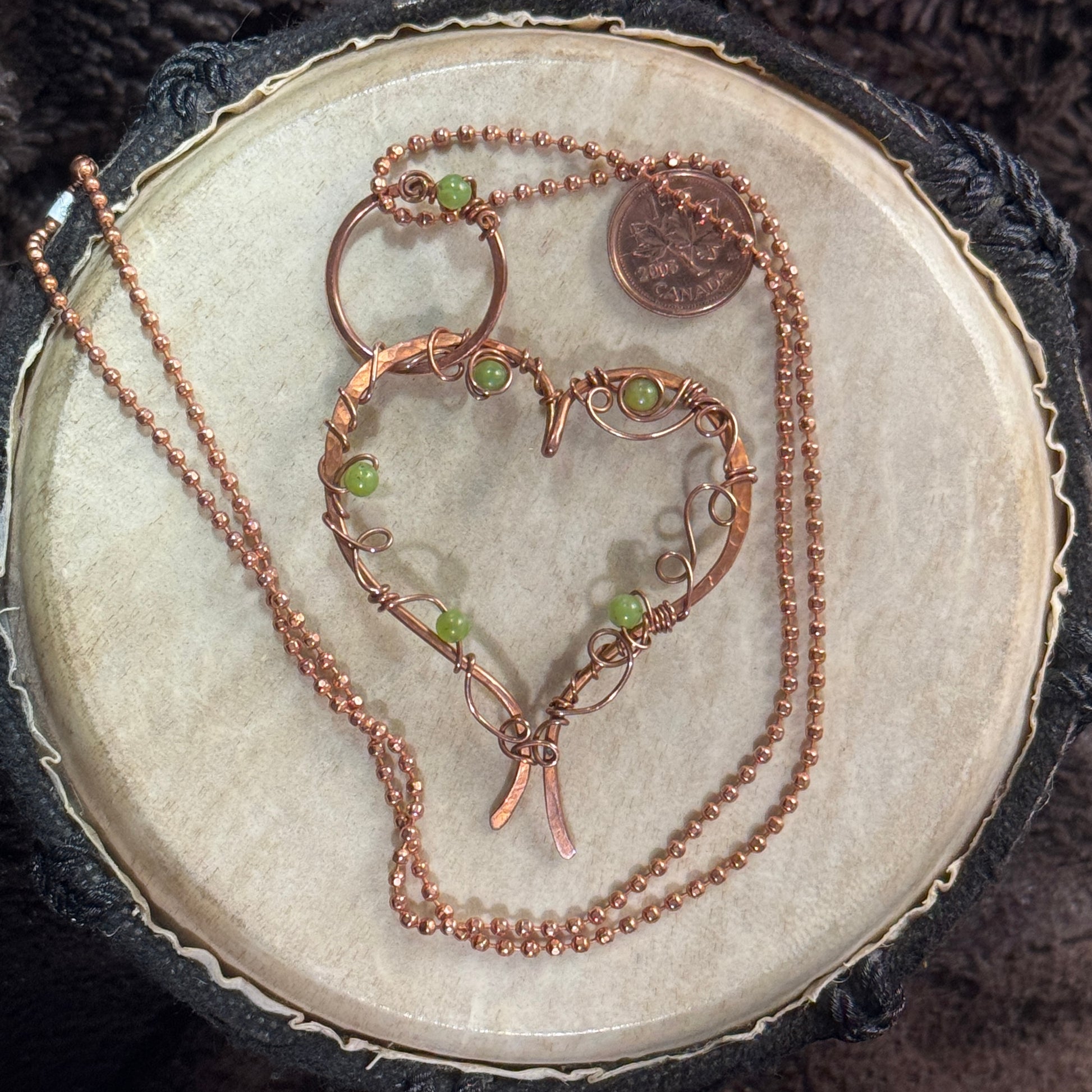 Handcrafted raw copper heart necklace with lemon jade beads on a 24 inch faceted copper ball chain, shown front facing on a natural display surface.