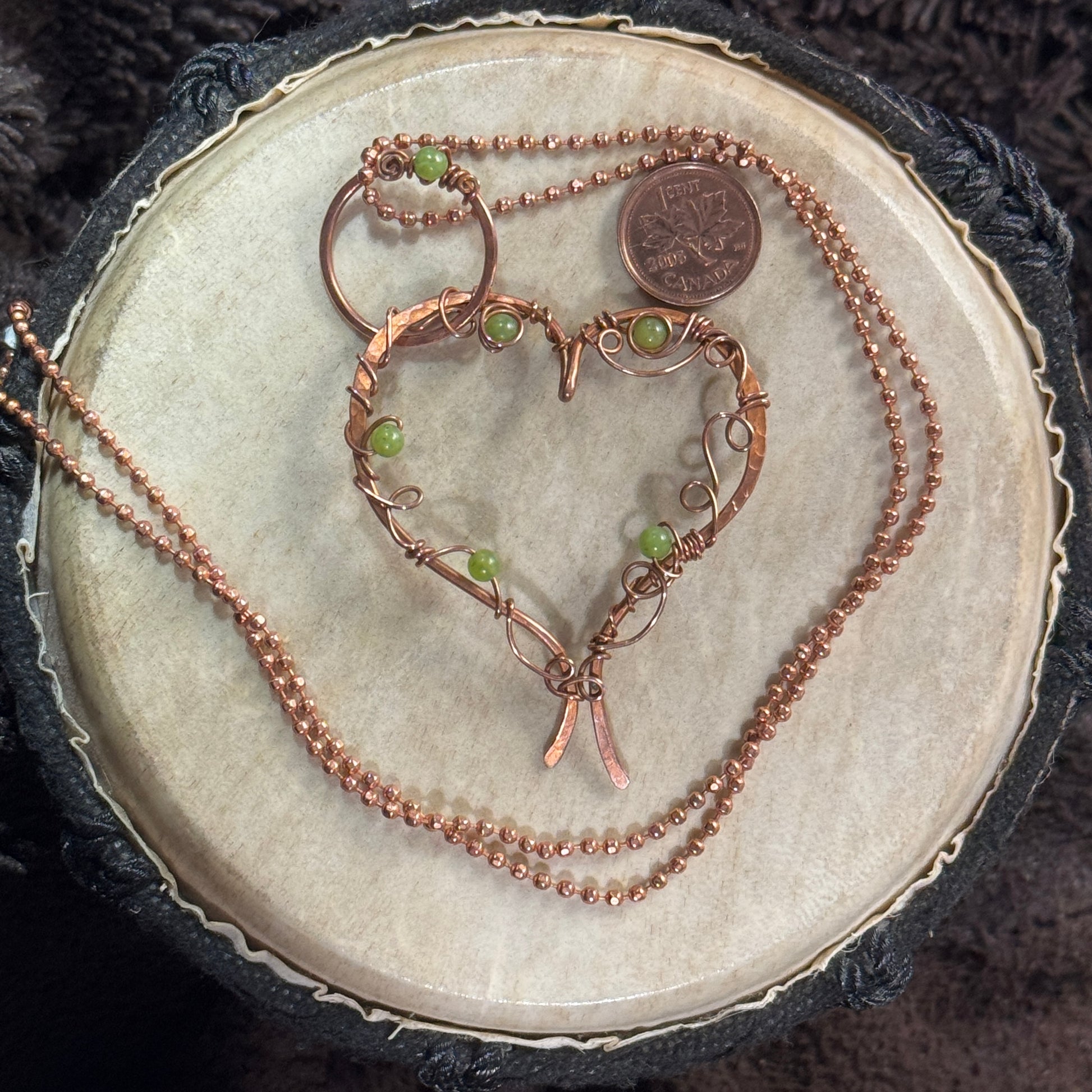Full view of a large open heart necklace in raw copper with lemon jade bead accents and a decorated jump ring on a copper ball chain.