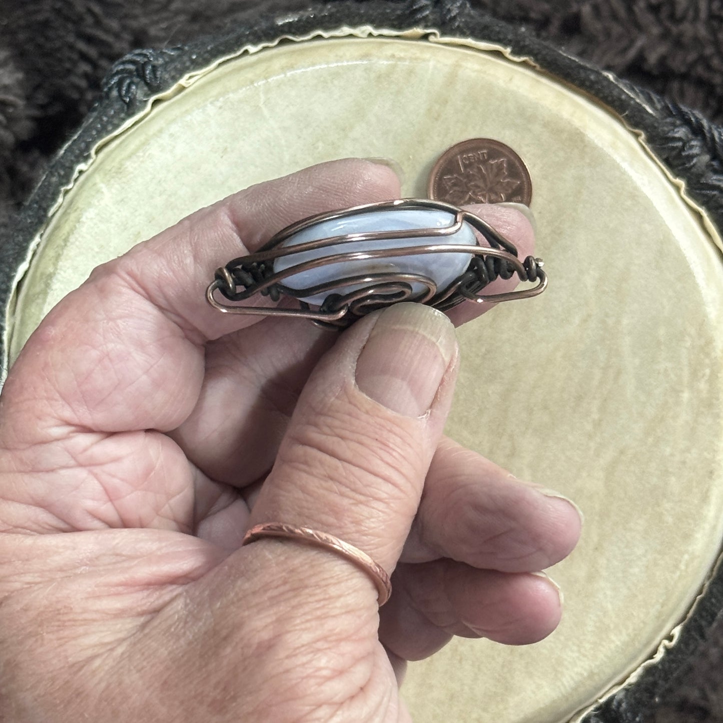 Hand-held side profile of a blue lace agate pendant showing the stone’s rounded depth, heavy 16-gauge copper framework and opposing bails.