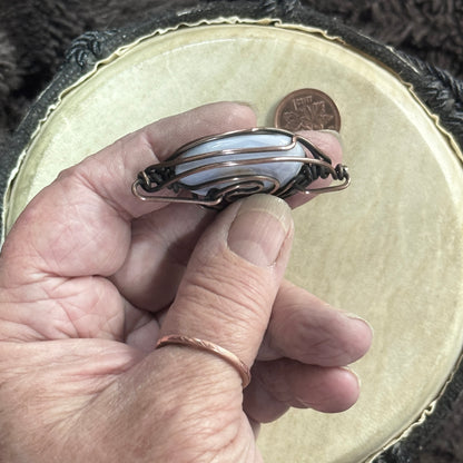 Hand-held side profile of a blue lace agate pendant showing the stone’s rounded depth, heavy 16-gauge copper framework and opposing bails.