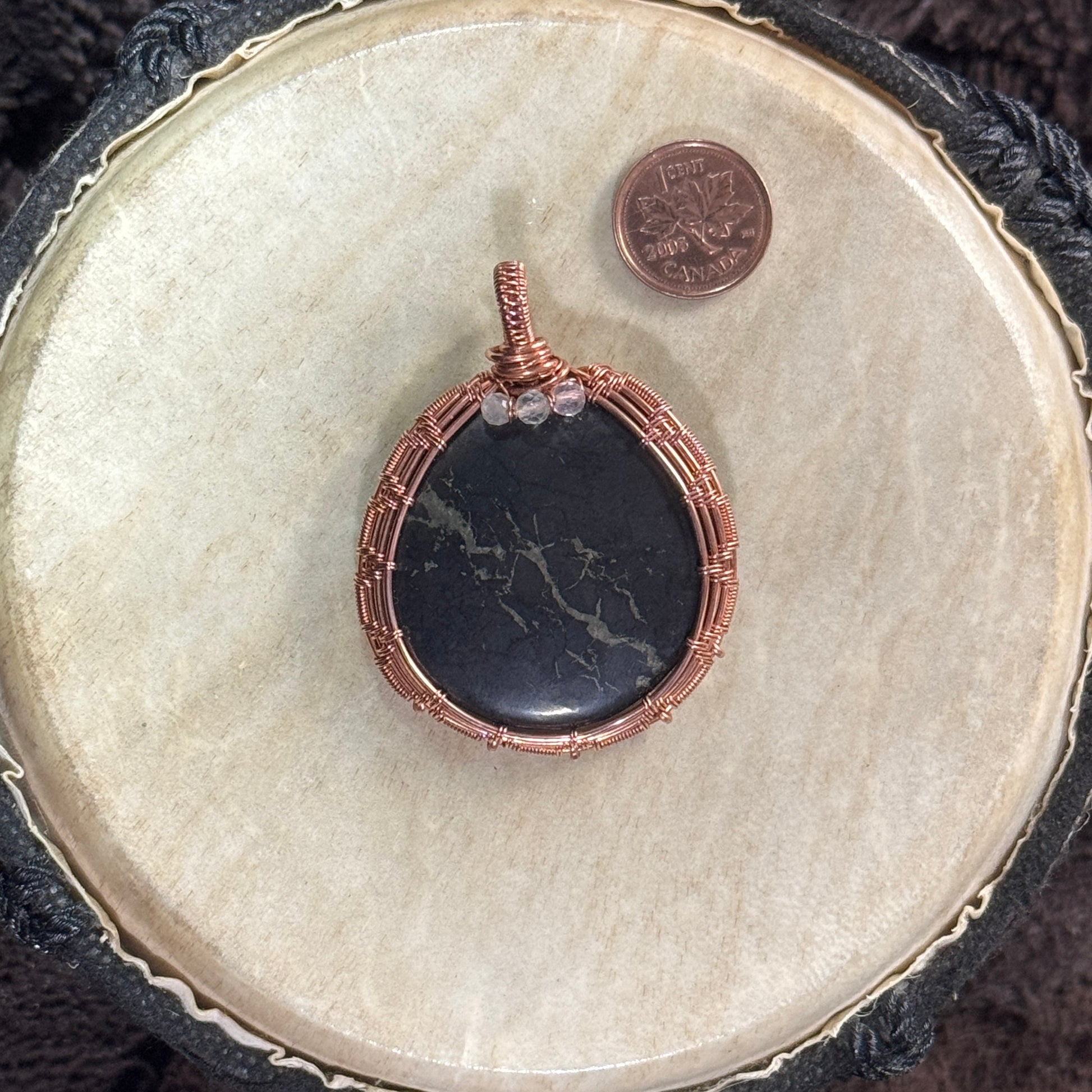 Front of a polished shungite pendant showing natural pyrite veining, three faceted fluorite beads and a structured handwoven raw copper frame.