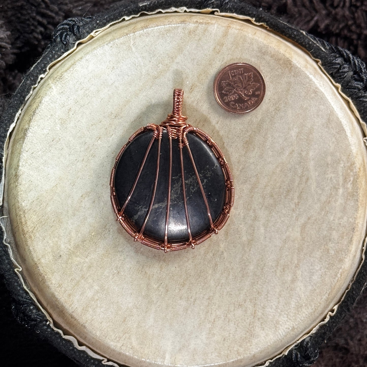 Back of a unisex shungite pendant showing radiating raw copper supports, detailed woven borders and the stone’s smooth rounded form.