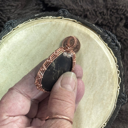 Hand-held side profile of a shungite pendant showing its substantial thickness, pyrite inclusion, faceted fluorite beads and woven copper bail.