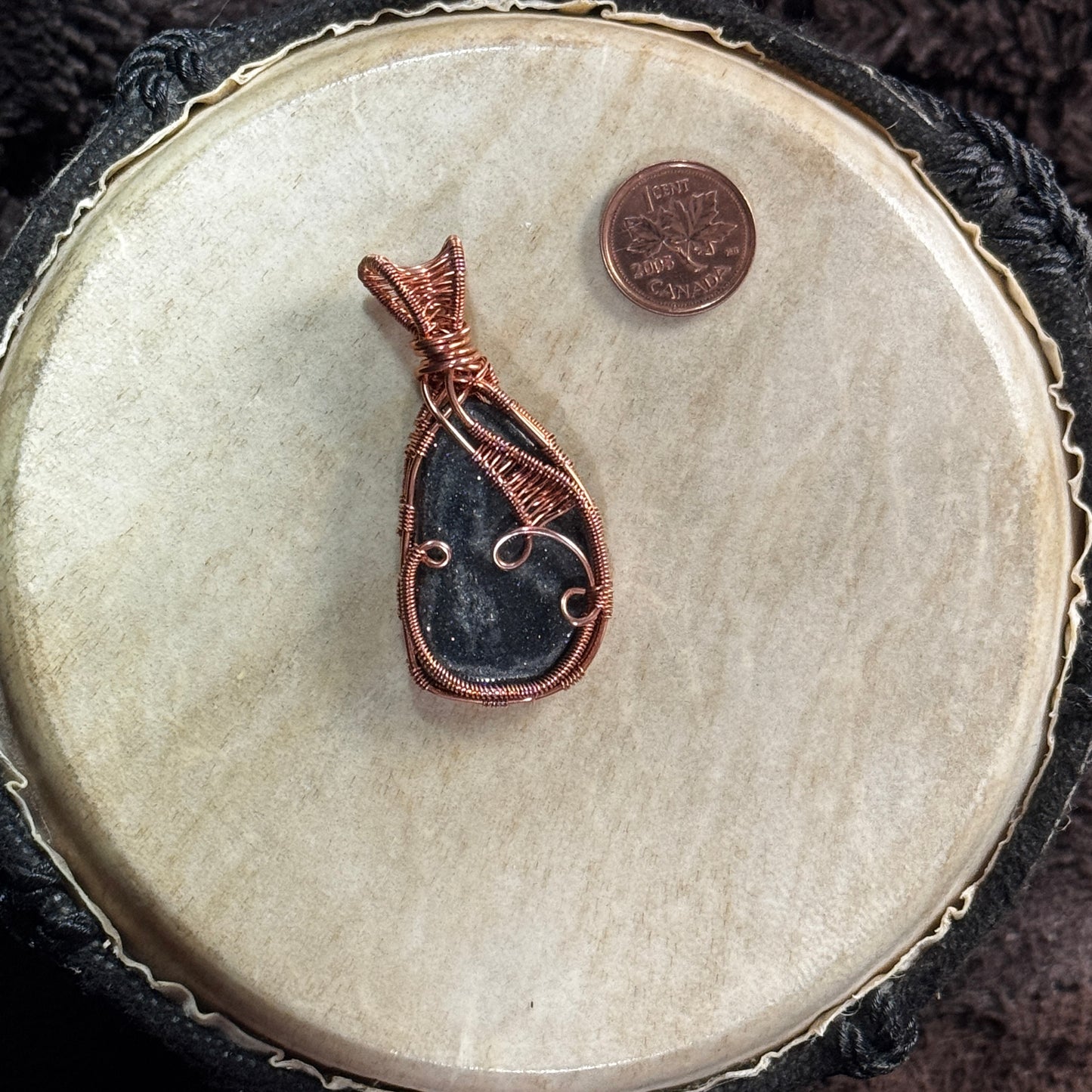 Side two of a reversible specular hematite pendant featuring an asymmetrical woven copper panel, open curls and a sculptural woven bail.