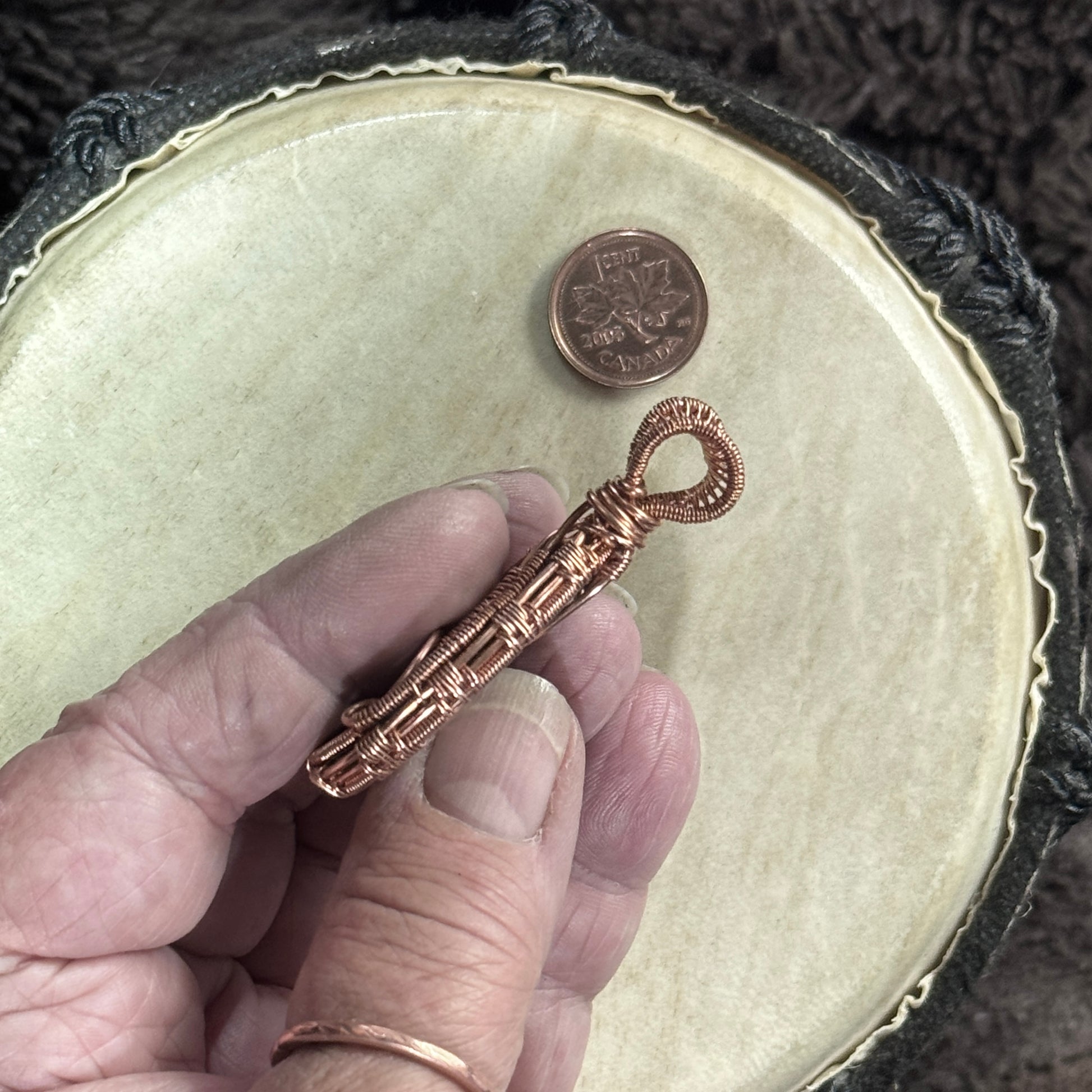 Hand-held side profile of a reversible specular hematite pendant showing the stone’s depth, woven raw copper edge and substantial open bail.