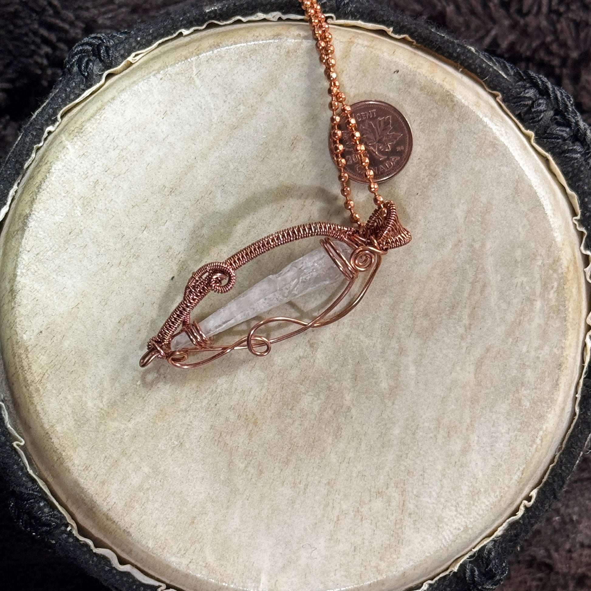 Angled profile of a Lemurian quartz point necklace showing its open copper framework, woven border and naturally tapered crystal form.