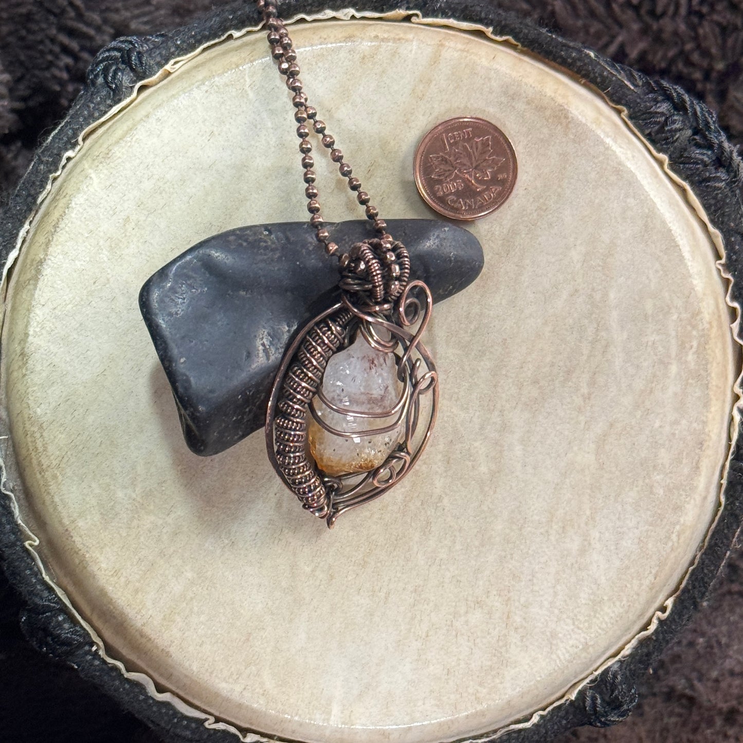 Raw citrine and hammered copper necklace styled against black shungite, highlighting its pale crystal body, golden tip and dense coilwork.
