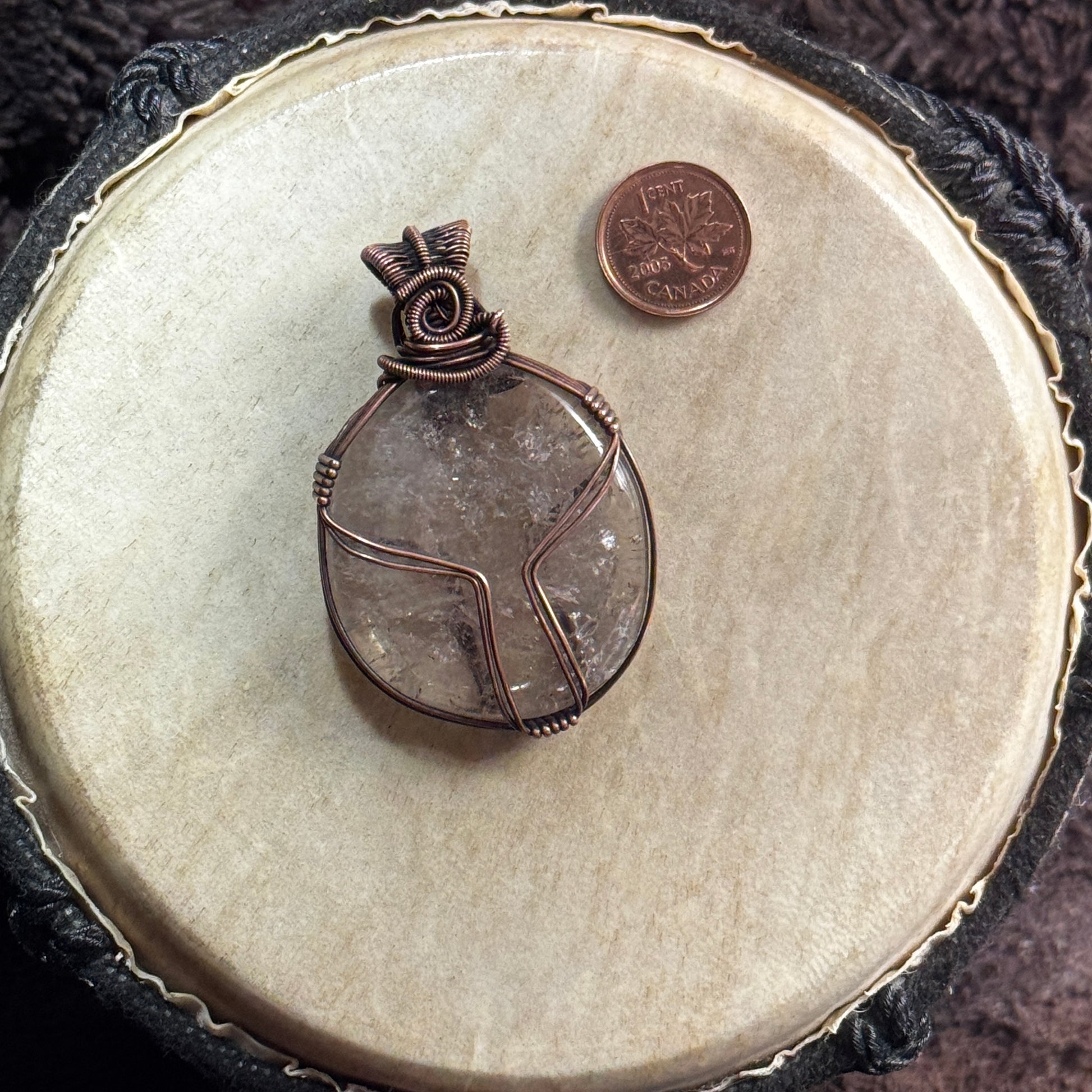 Side one of a reversible oval smoky quartz pendant wrapped in patinated copper with strong geometric lines and a tightly woven spiral bail.