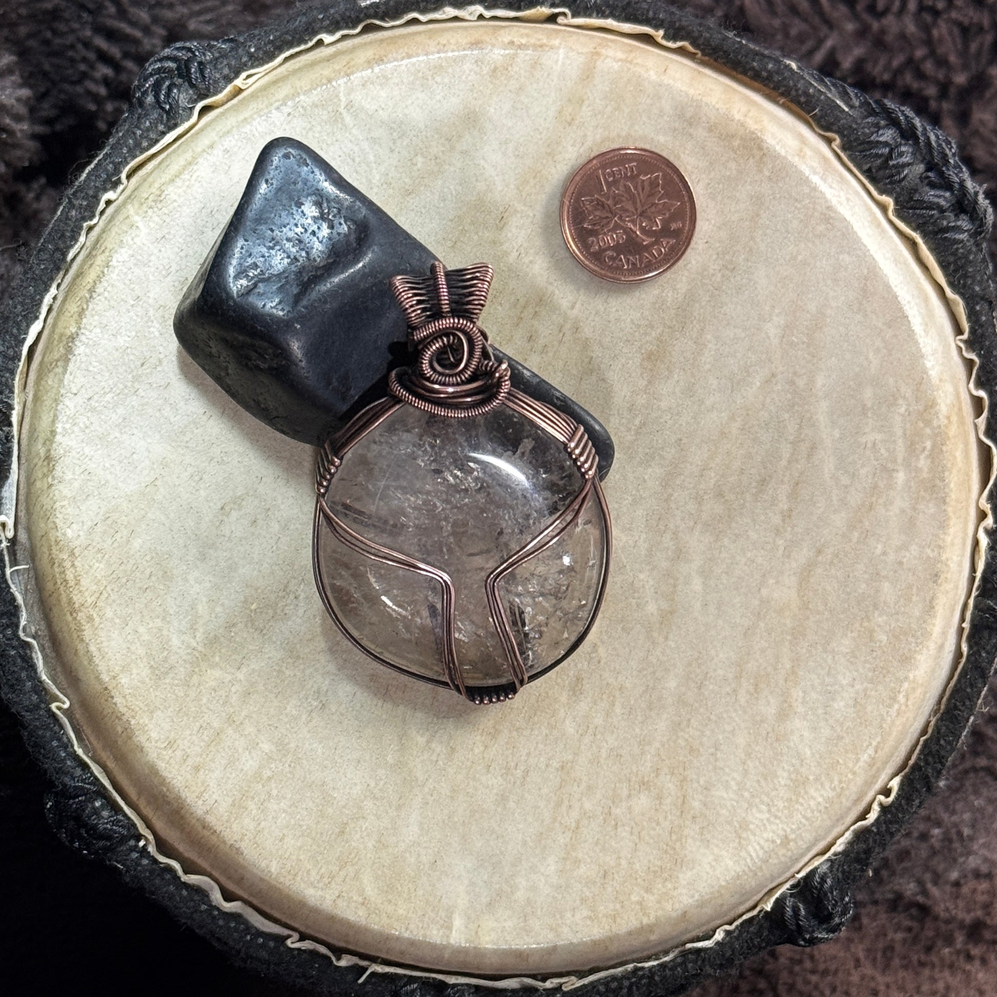 Reversible smoky quartz and patinated copper pendant styled against black shungite, with a Canadian penny included for scale.