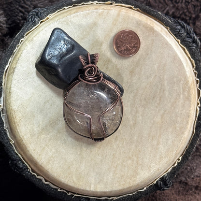 Reversible smoky quartz and patinated copper pendant styled against black shungite, with a Canadian penny included for scale.