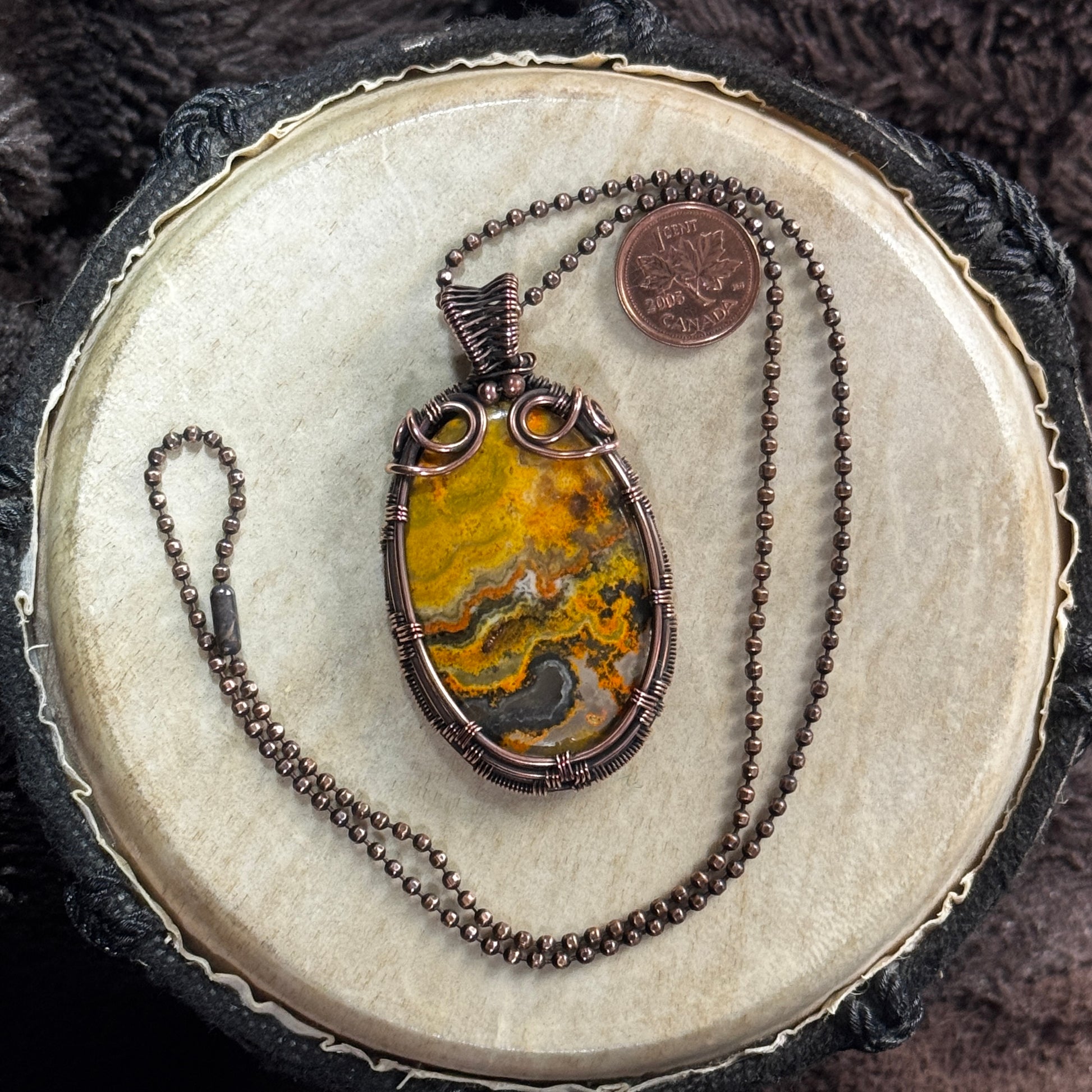 Front view of a yellow, orange, grey and black Bumble Bee Jasper cabochon wrapped in patinated copper on a 20-inch faceted ball chain.