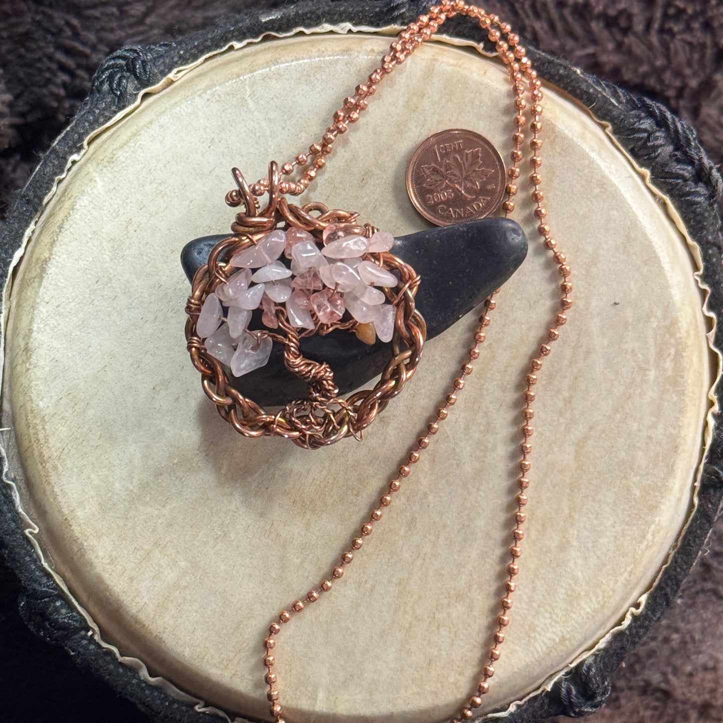 Rose quartz and reclaimed copper Tree of Life necklace styled over black shungite with its faceted copper ball chain and penny shown for scale.