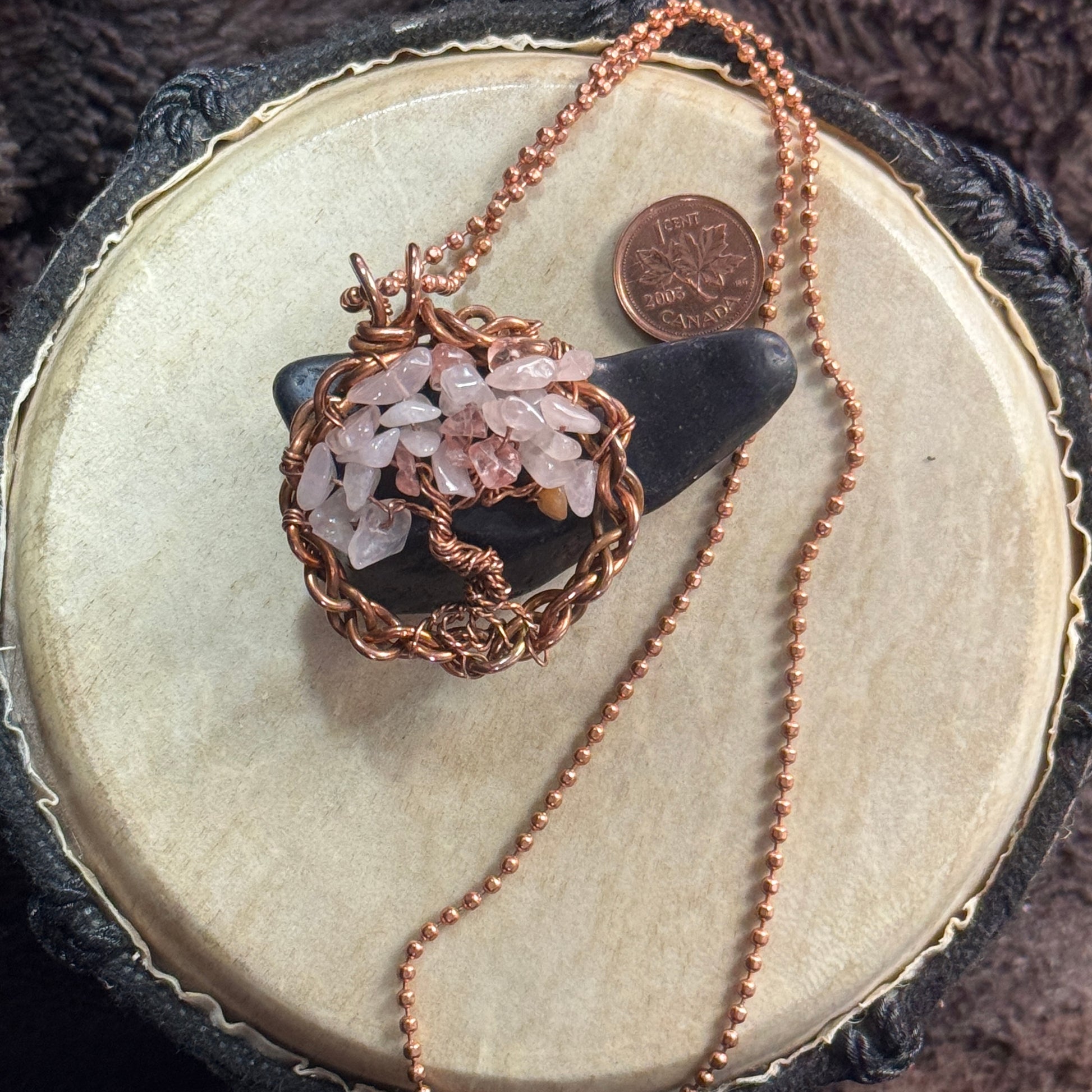 Rose quartz and reclaimed copper Tree of Life necklace styled over black shungite with its faceted copper ball chain and penny shown for scale.