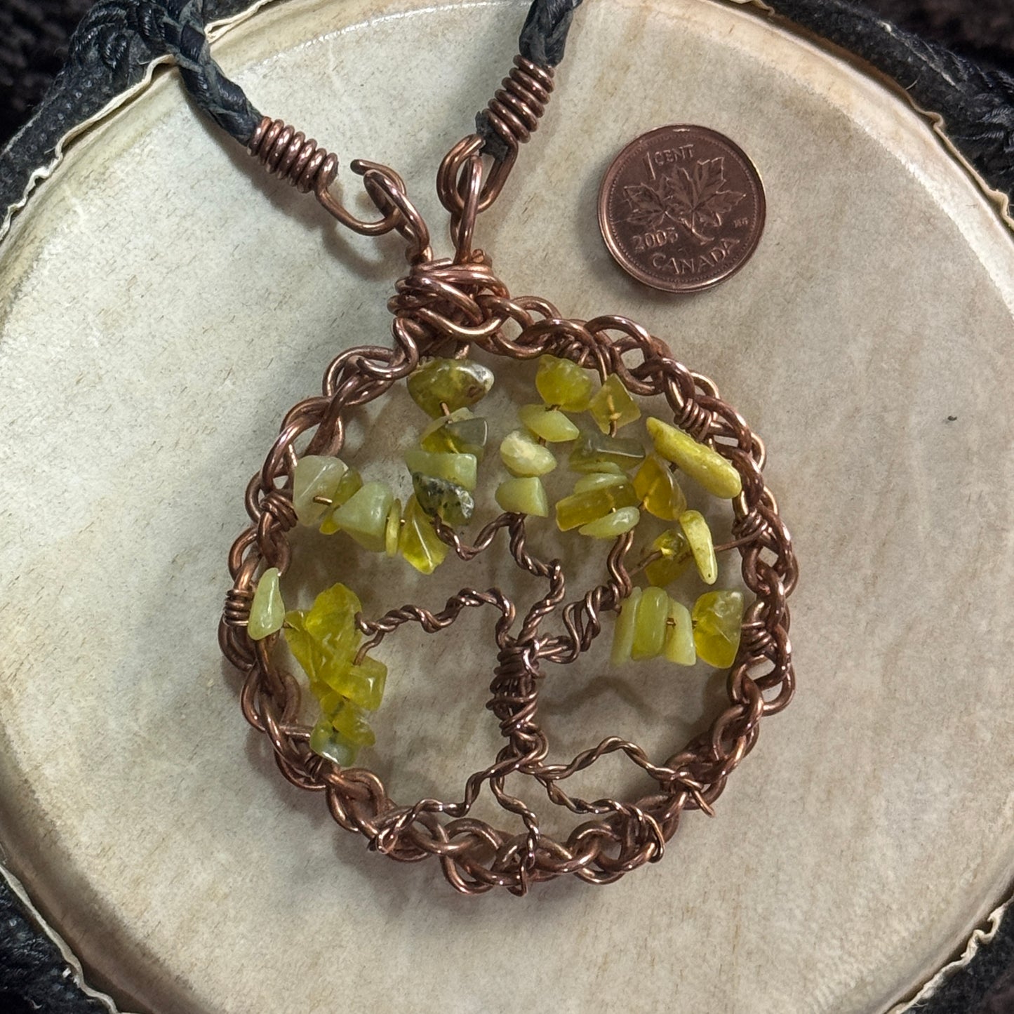 Close-up of yellow-green lemon jade chips forming the canopy of a hand-twisted raw copper Tree of Life with a woven circular frame.