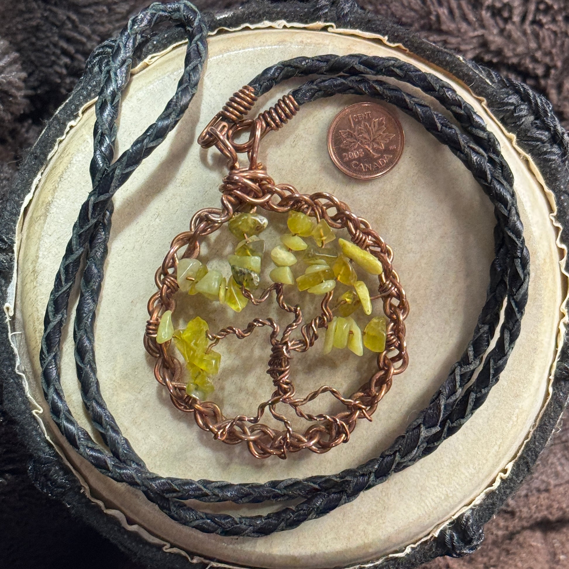 Lemon jade Tree of Life necklace displayed with its reclaimed braided leather cord and front copper closure beside a Canadian penny for scale.