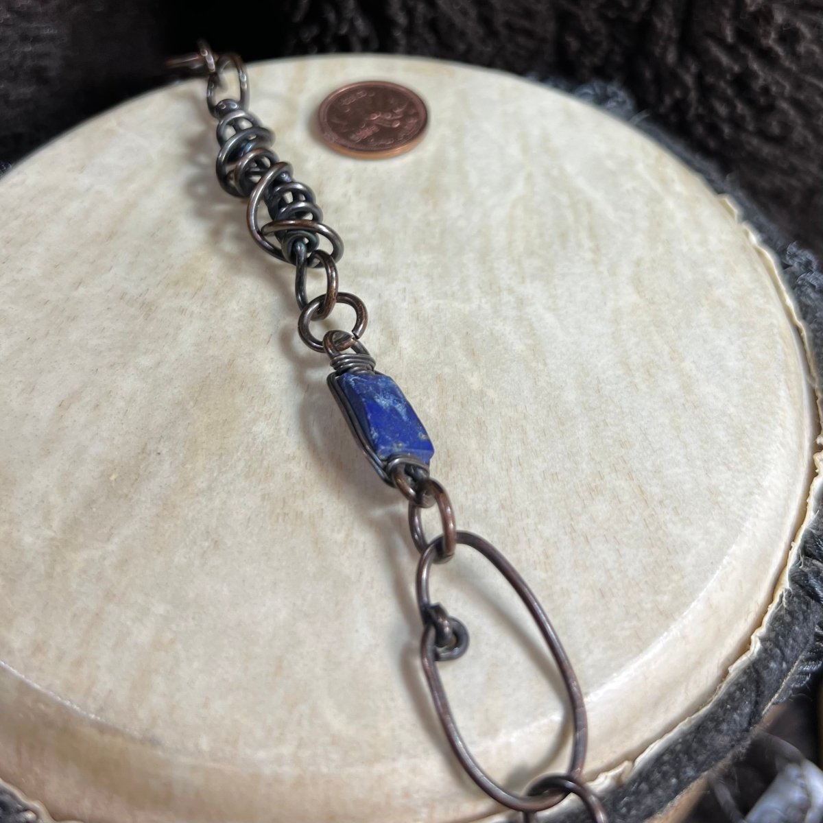 Handmade patinated copper opera necklace with lapis lazuli stones and woven wire focal element, photographed with Canadian penny for scale.