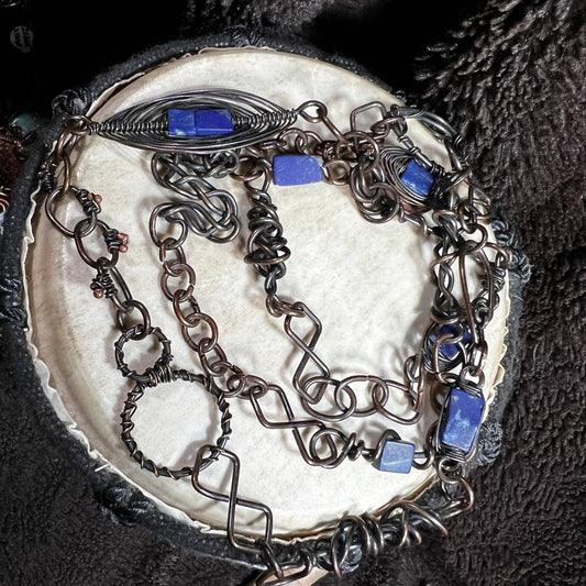 Handmade patinated copper opera necklace with lapis lazuli stones and woven wire focal element, photographed with Canadian penny for scale.