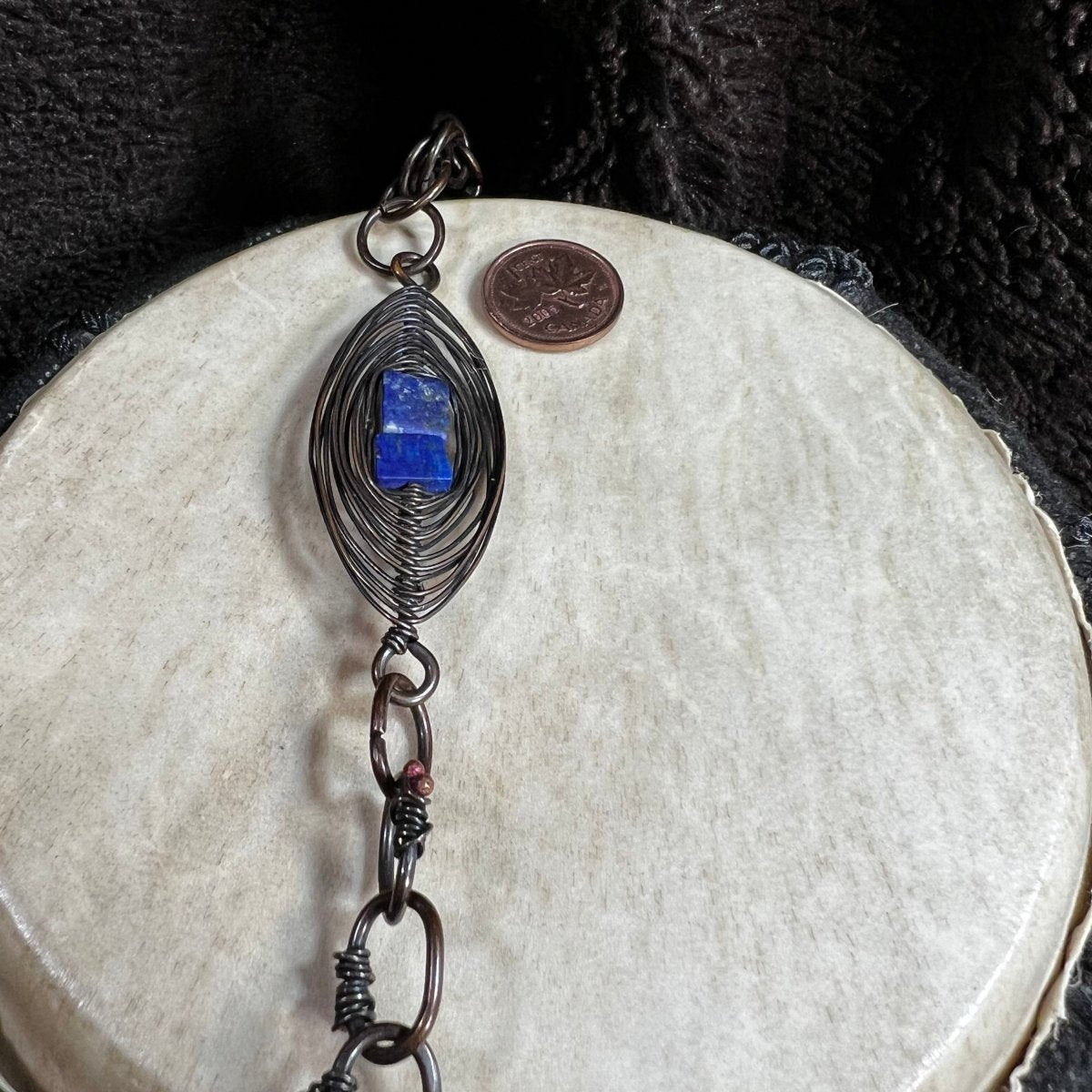 Handmade patinated copper opera necklace with lapis lazuli stones and woven wire focal element, photographed with Canadian penny for scale.