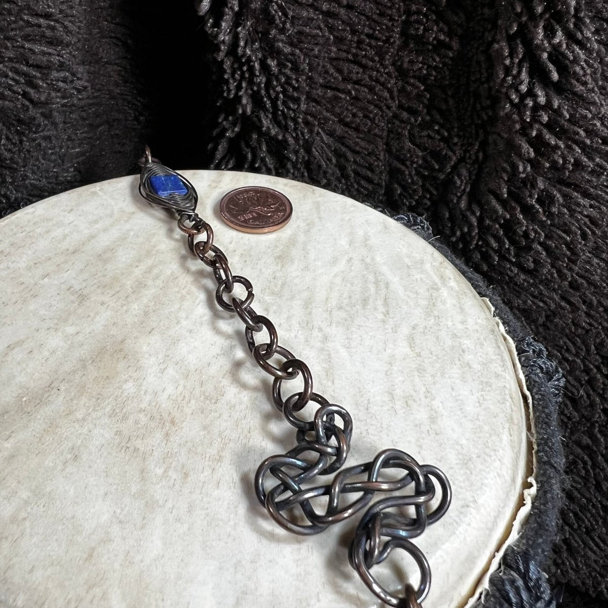 Handmade patinated copper opera necklace with lapis lazuli stones and woven wire focal element, photographed with Canadian penny for scale.
