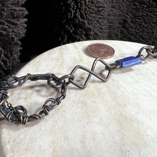 Handmade patinated copper opera necklace with lapis lazuli stones and woven wire focal element, photographed with Canadian penny for scale.