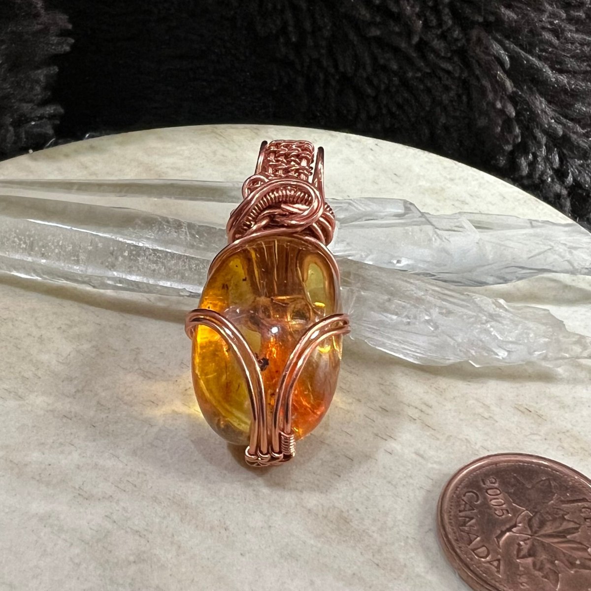 amber pendant displayed with clear quartz crystals, handmade copper wire wrapped jewellery with glowing golden stone