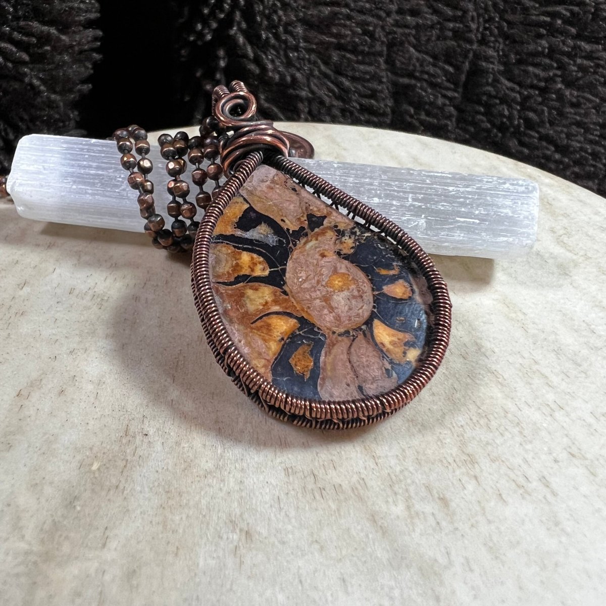 Close-up of ammonite fossil shell pendant in copper wire wrap, ancient fossil jewelry
