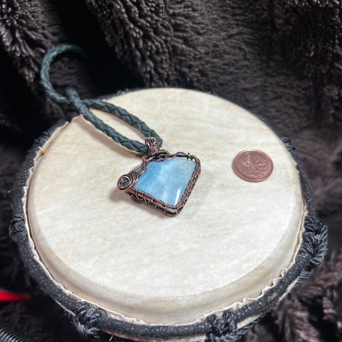 Aquamarine stone necklace on a circular surface against a dark textured background, next to a penny for scale.