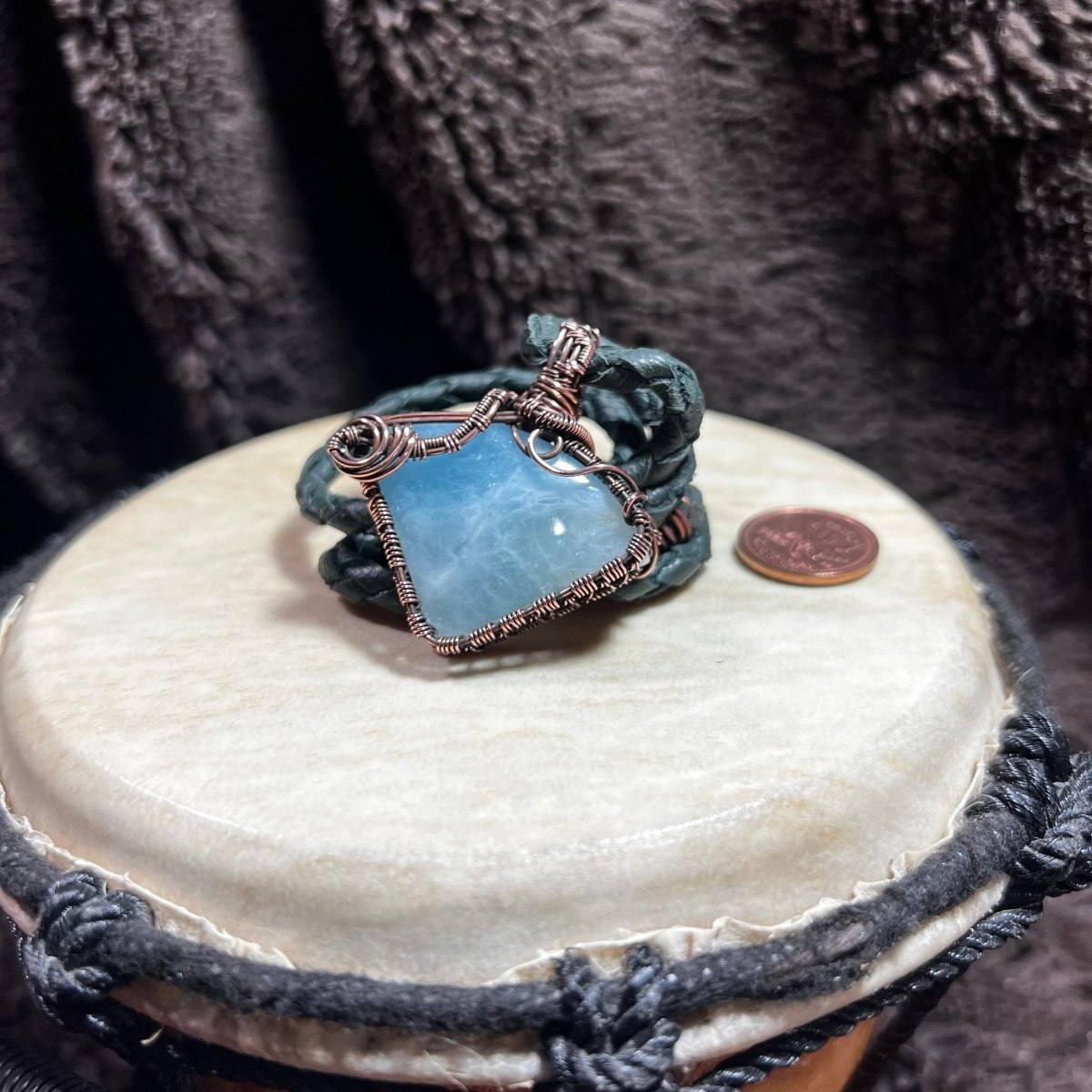 Blue stone necklace with copper wire wrapping on a textured surface