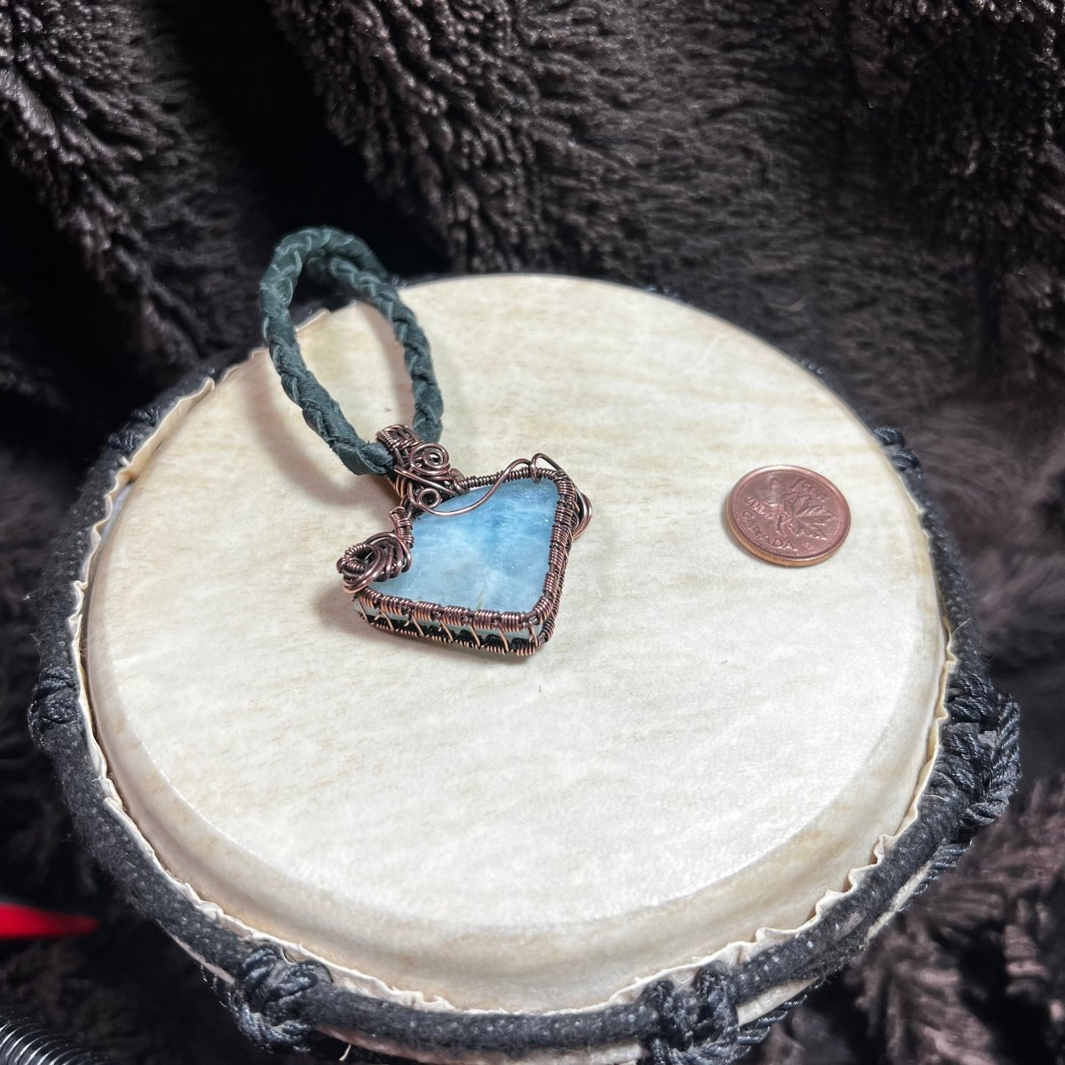 Blue stone pendant on a textured surface with a penny for scale