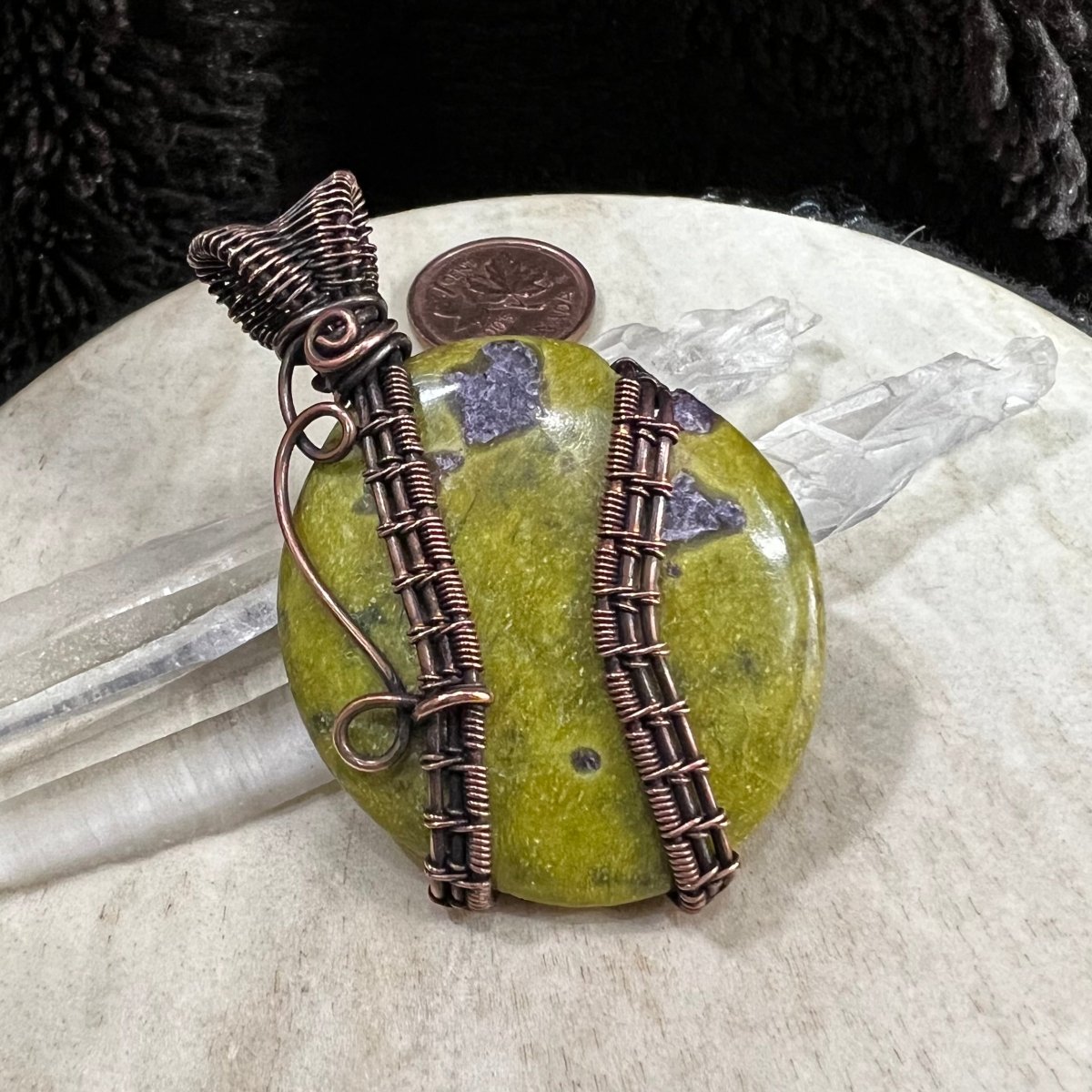 Atlantisite pendant displayed with quartz crystals and a Canadian penny  for scale and earthy colour contrast