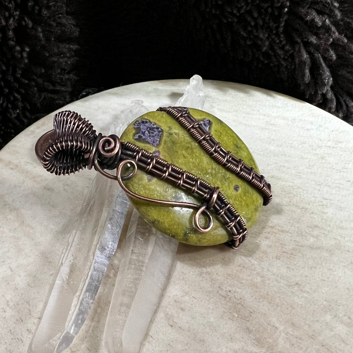 Close-up of Atlantisite stone showing natural green and violet patterns with protective copper wire wrap