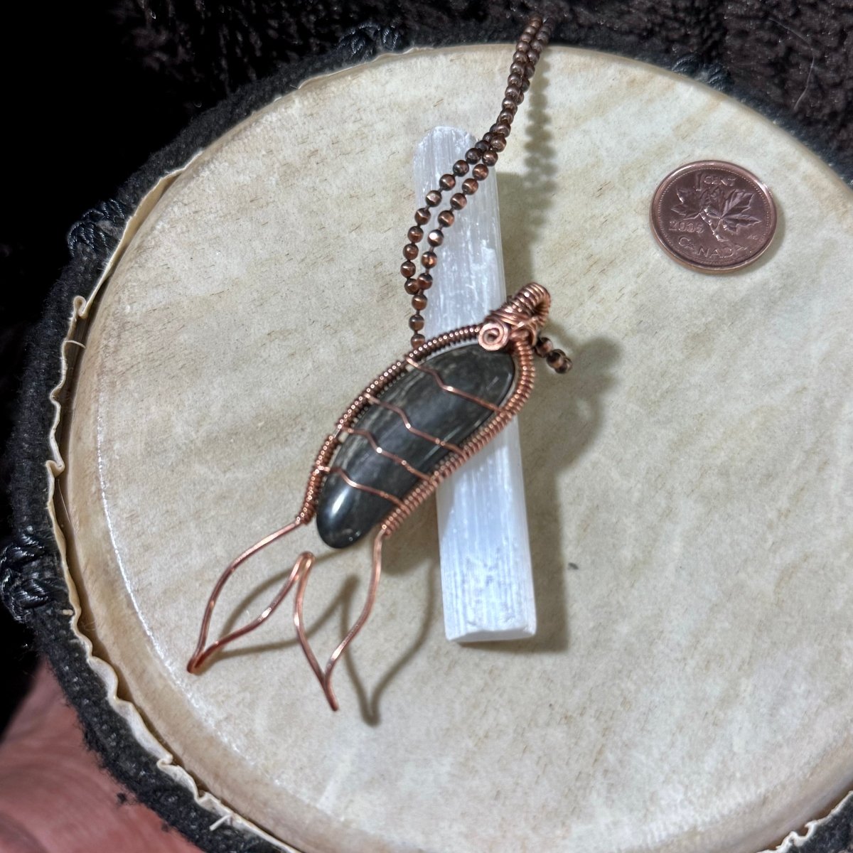 Black agate Mermaid Tail necklace displayed on a selenite wand, showcasing the dark banding of the Bay of Fundy stone and handcrafted reclaimed copper details.