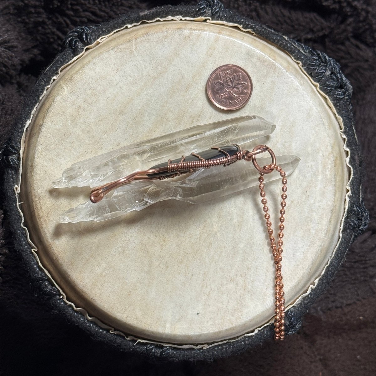 Side profile of a handmade black agate Mermaid Tail pendant in raw copper displayed with clear crystal points.