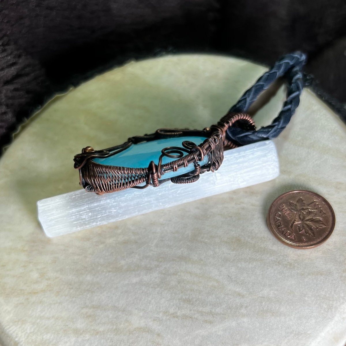 Blue Aragonite pendant side view with copper wire wrapping on a beige surface next to a penny for scale.