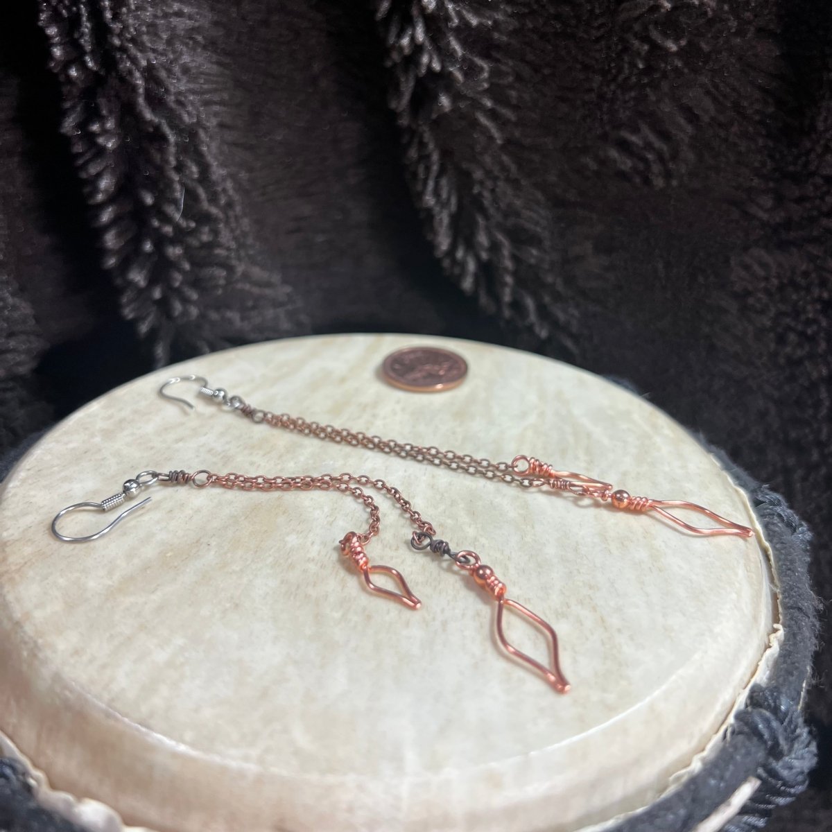 Pair of copper chain earrings on a round stone surface with a penny for scale.