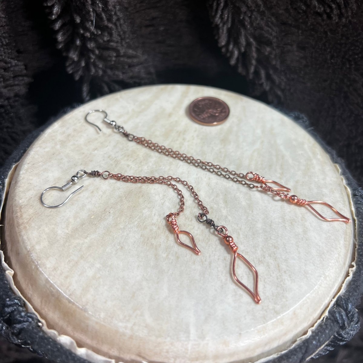 Pair of copper chain earrings on a round stone surface with a penny for scale.