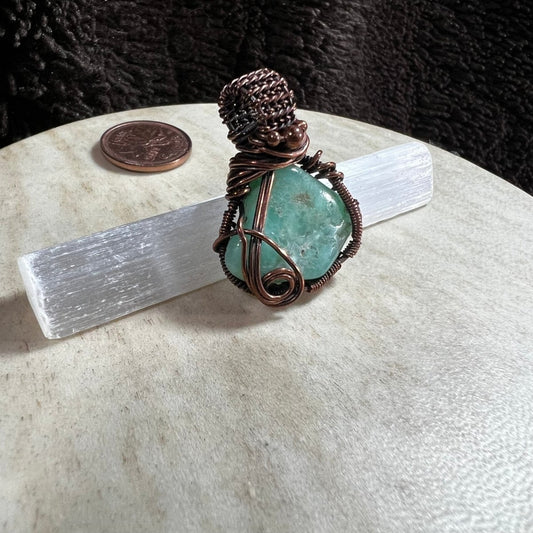 Handmade Chrysoprase pendant wrapped in reclaimed copper wire resting on a selenite wand with penny for size reference.