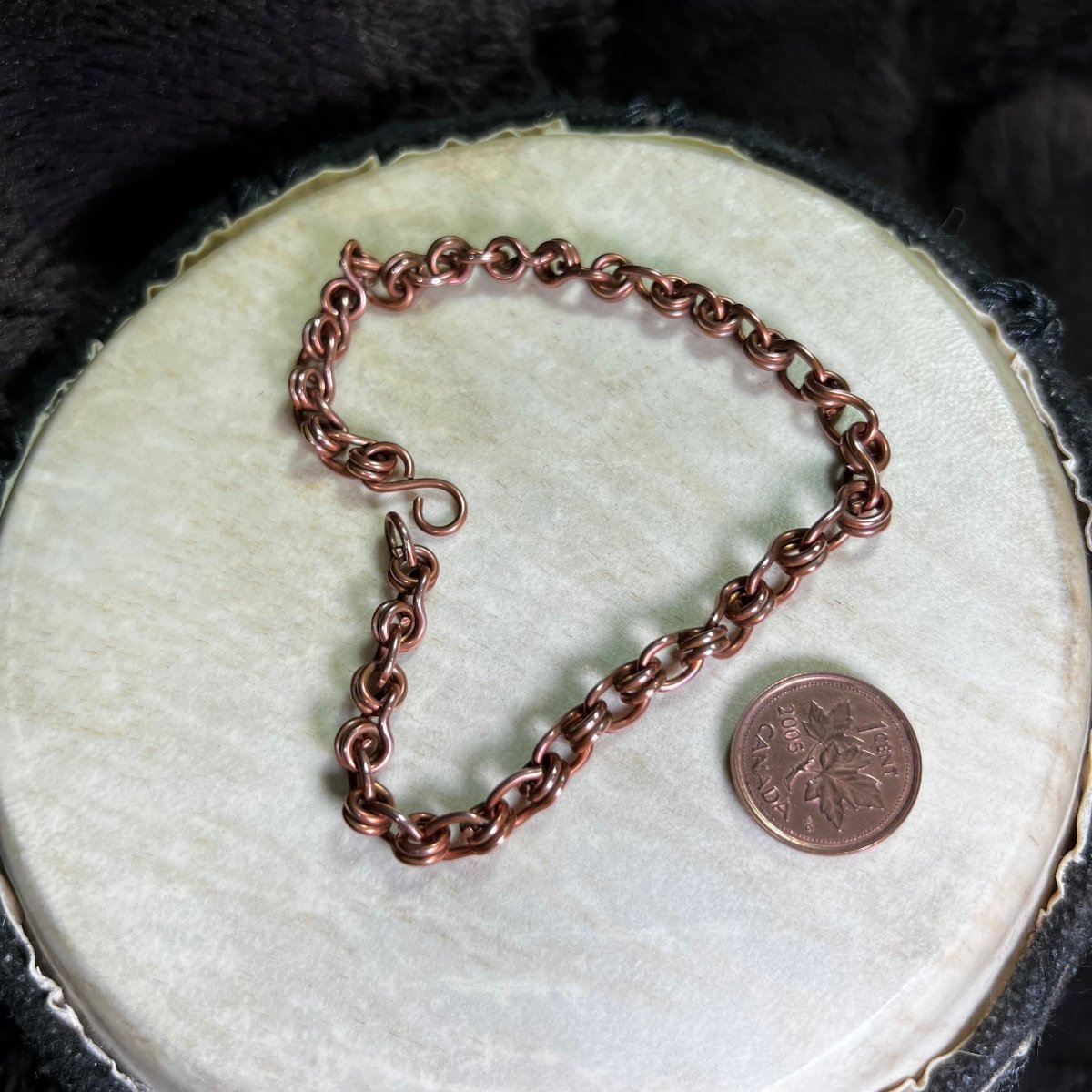 Copper chain bracelet on a white surface with a penny for scale