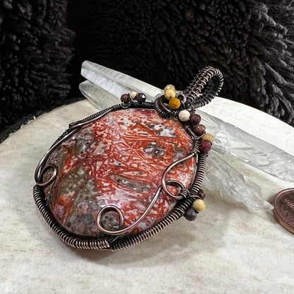Crazy Lace agate palm stone with copper wire wrapping and mookaite accent beads on a neutral surface