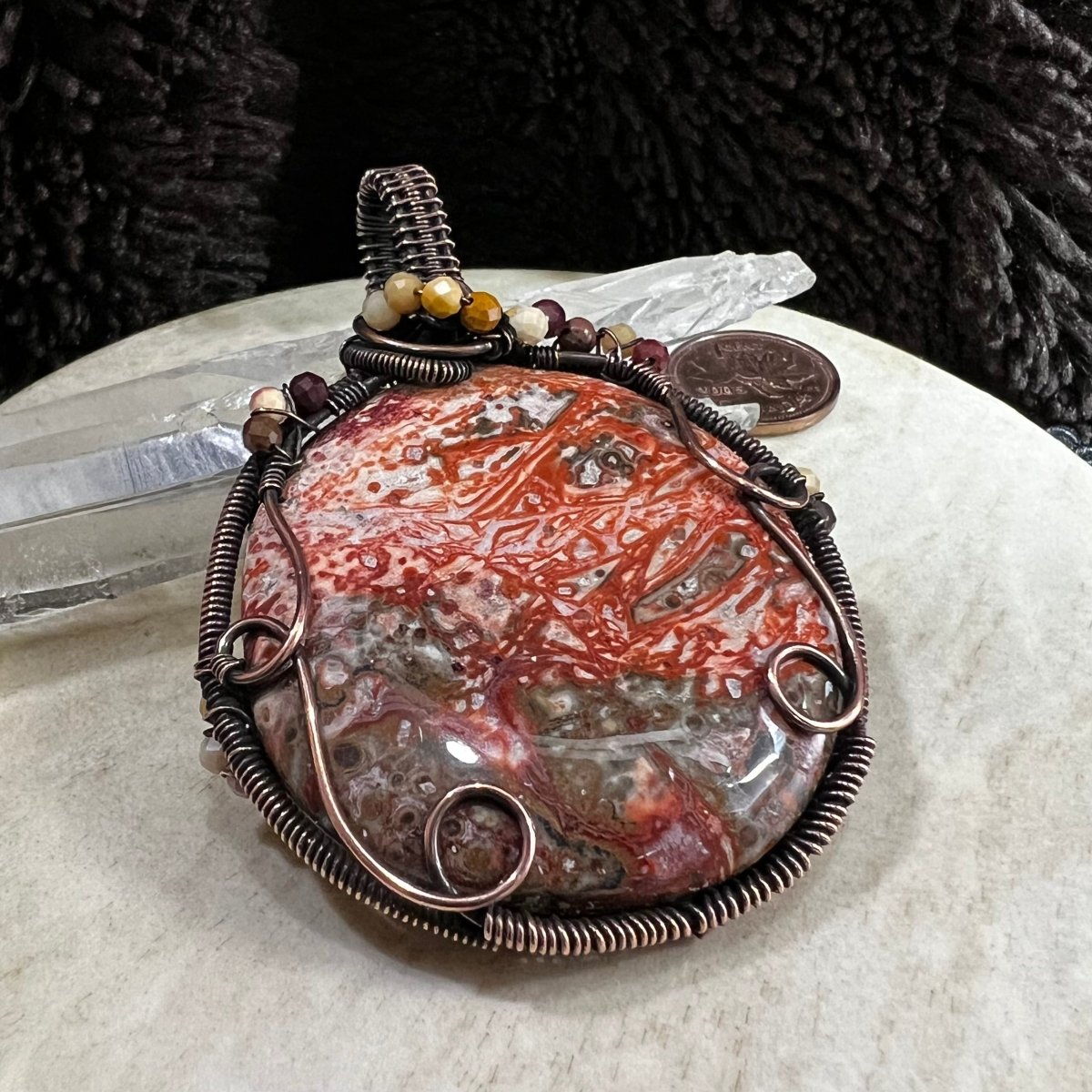 crazy lace agate pendant with patinated copper wire wrapping on a beige surface
