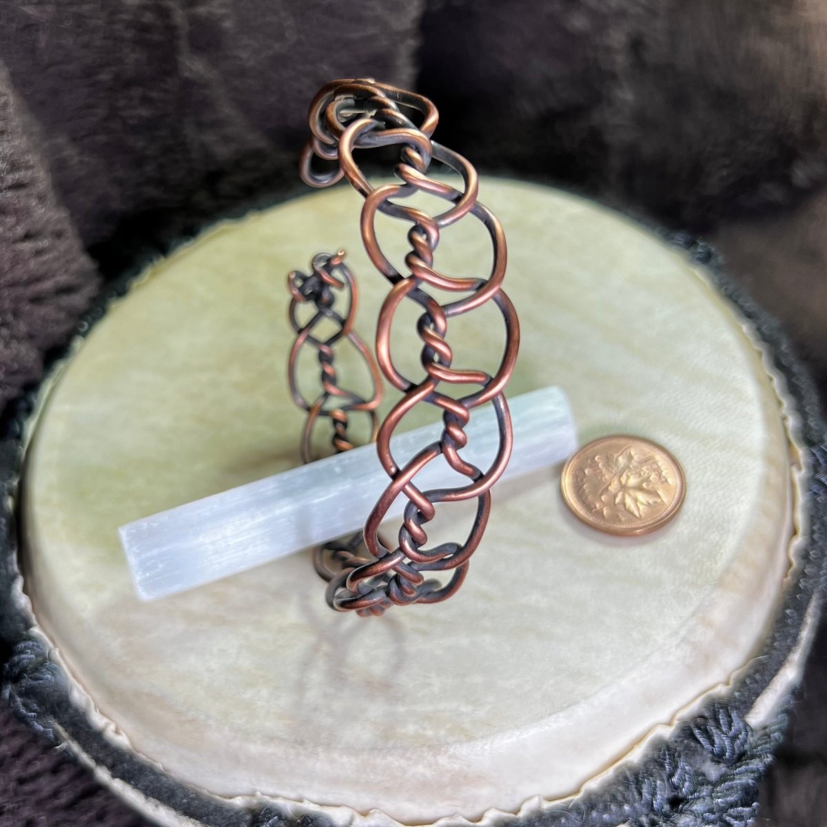 Copper bracelet on a beige surface with a coin and crystal