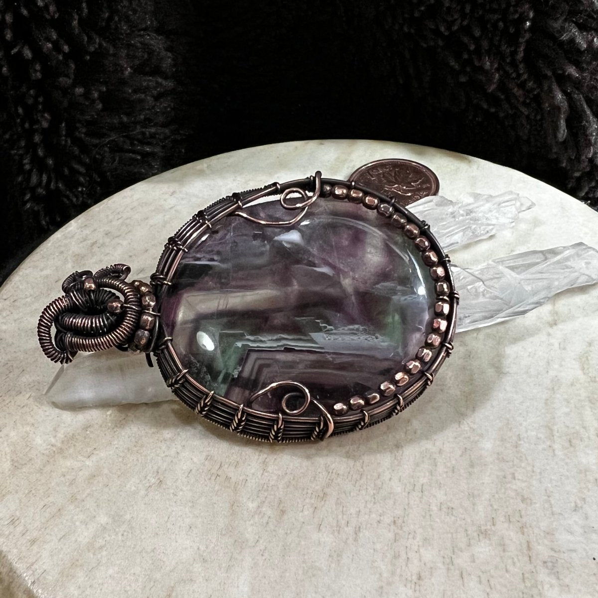 Fluorite copper pendant displayed with quartz crystals for scale and soft natural contrast