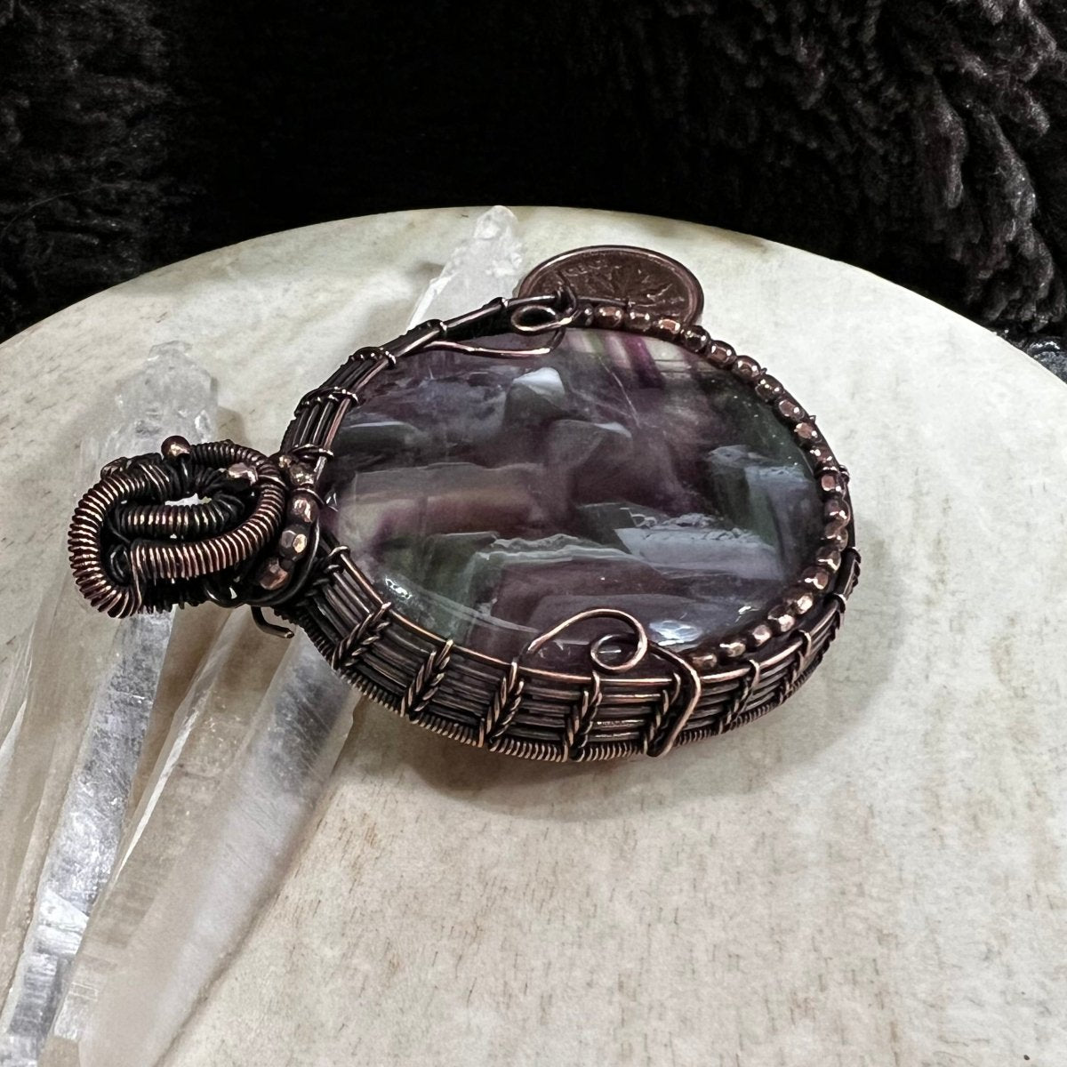 Close-up of fluorite pendant showing layered colour bands and polished surface with copper wire detail