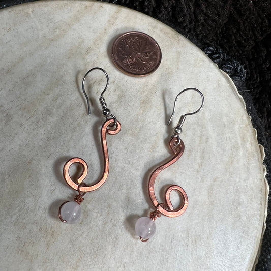 Handmade hammered copper spiral earrings with rose quartz bead drops and surgical steel ear wires, photographed with Canadian penny for scale.