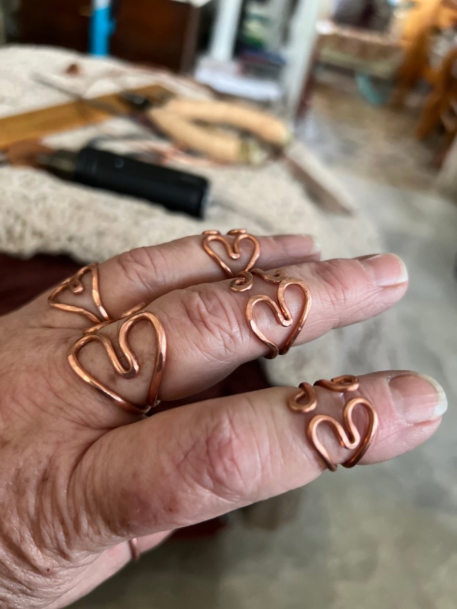 Close-up of a hand wearing multiple copper heart-shaped rings with a blurred background.