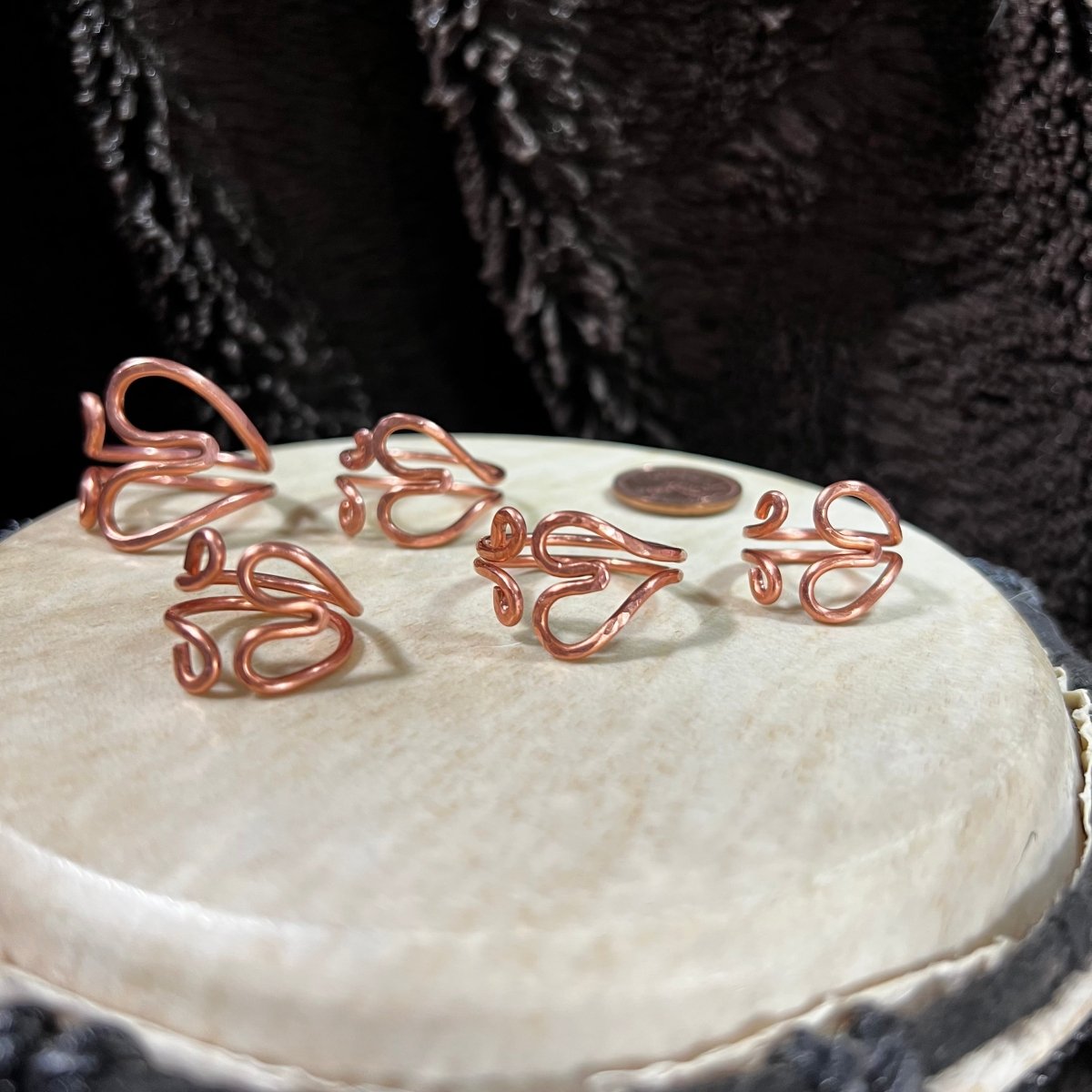 Reclaimed copper wire heart-shaped rings on a white surface with a black background