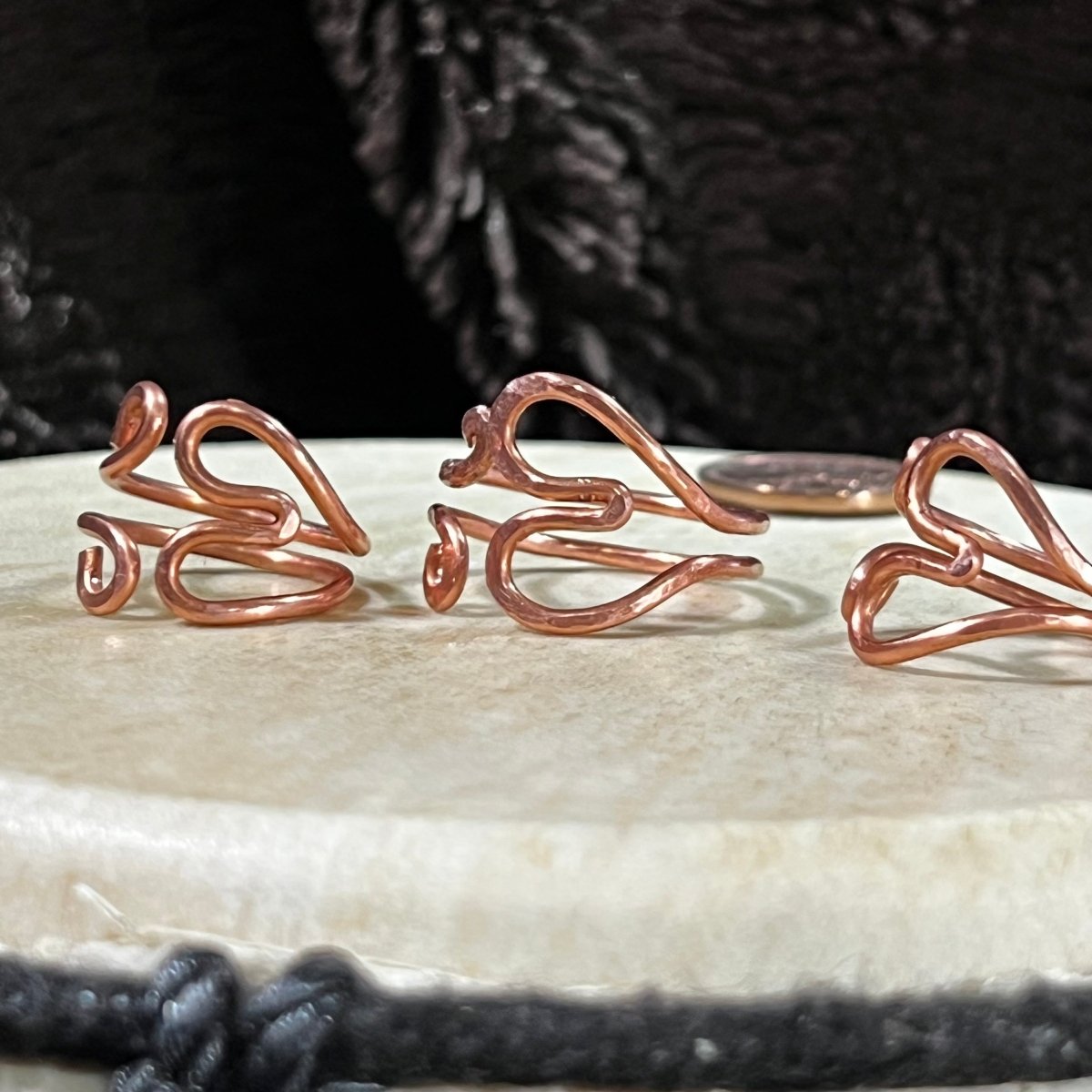 Reclaimed copper wire heart-shaped rings on a white surface with a black background