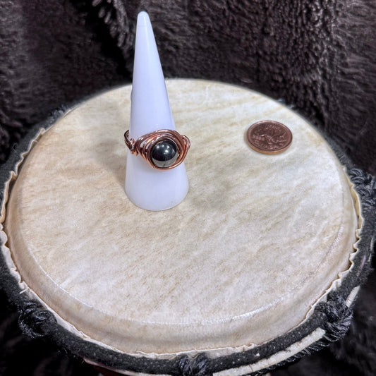 Front view of a polished metallic hematite sphere wrapped in bright reclaimed copper as a handmade size 10 ring.
