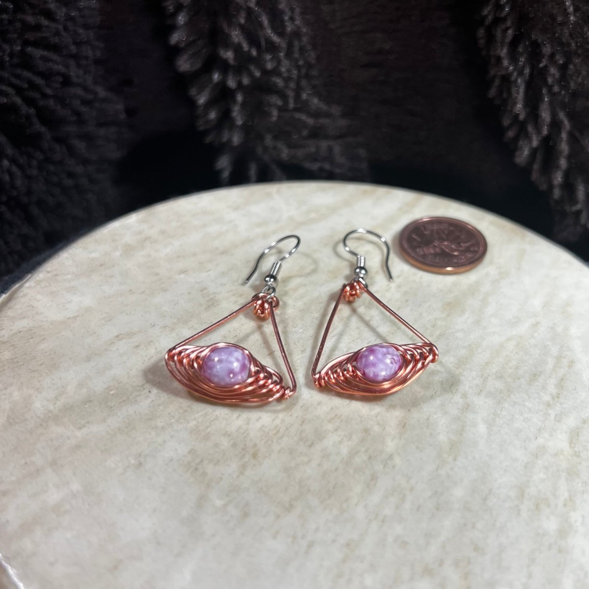Pair of wire-wrapped earrings with pink purple stones on a round stone surface.