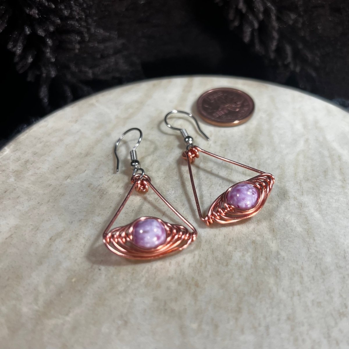 Copper wire earrings with pink and purple beads on a stone surface